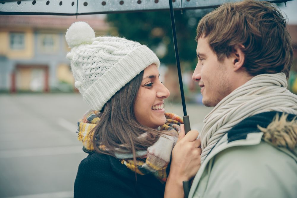 Happy couple facing each other under the umbrella on an autumn rainy day