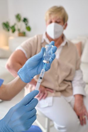 Crop doctor filling syringe with vaccine against mature patient
