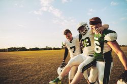 Two footballers carrying an injured teammate off the field