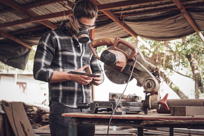 Male carpenter wearing protective mask in workshop measuring wood