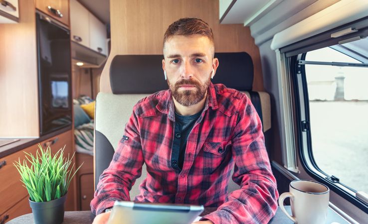 Man in red checkered shirt sitting in van with digital tablet and coffee
