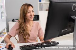 Confident Asian woman sitting in office and using computer while looking at monitor 5XqWQ4