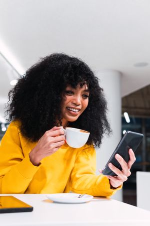 Smiling woman messaging on smartphone and drinking coffee in cafe