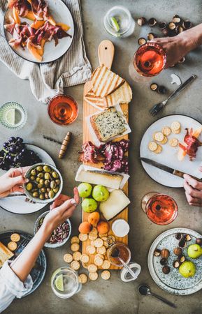 Charcuterie board with hands holding olive bowl and glass of rose