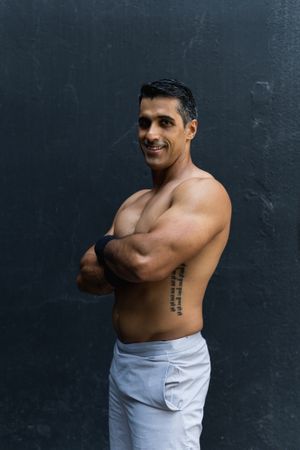 Positive shirtless Hispanic sportsman near wall