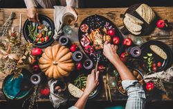 Autumnal table with squash and candles with man carving roast chicken and woman holding wine