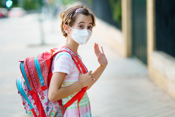 Girl waves while wearing mask and backpack