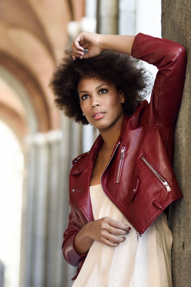 Woman standing in archway in red leather jacket and her hand up