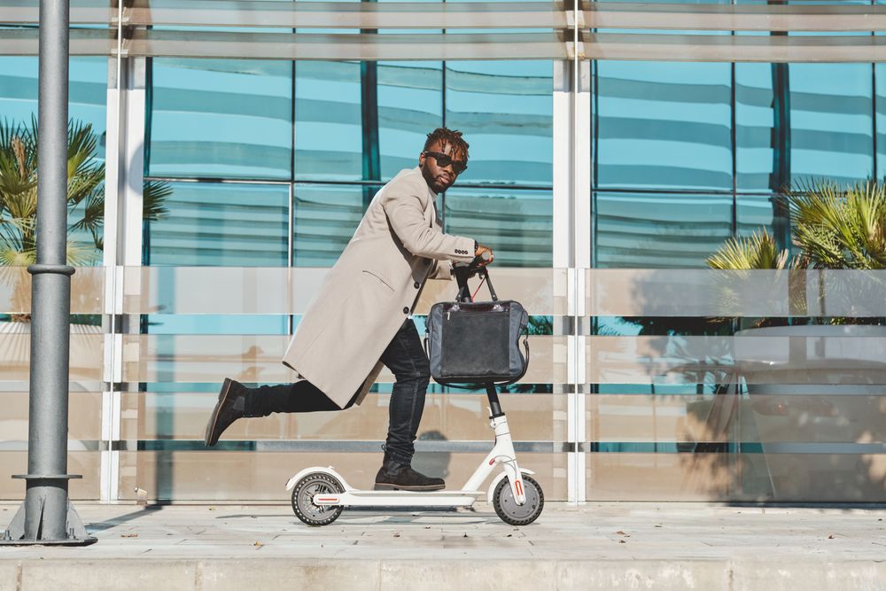 Stylish Black man with handbag riding scooter