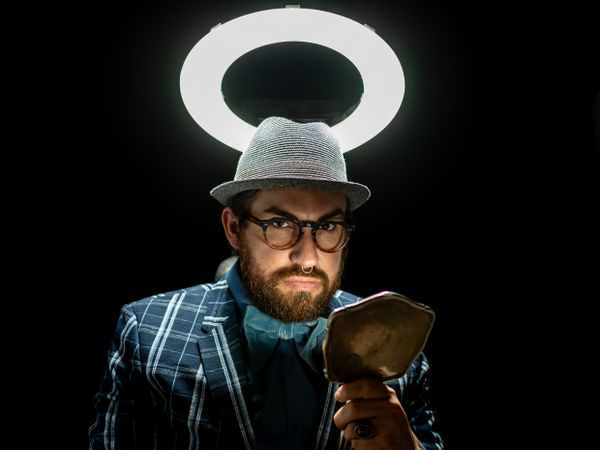 Fashion man in hat holding hand mirror and looking at camera