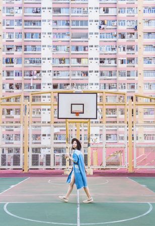 Woman in blue dress standing in basketball court beside a building