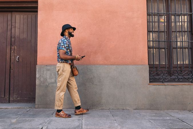 Stylish Black man walking on the city street using smartphone