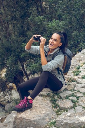 Cheerful woman tourist on rocky terrain and looking at binocular