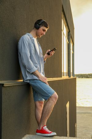 Young man in headphones listen music against wall