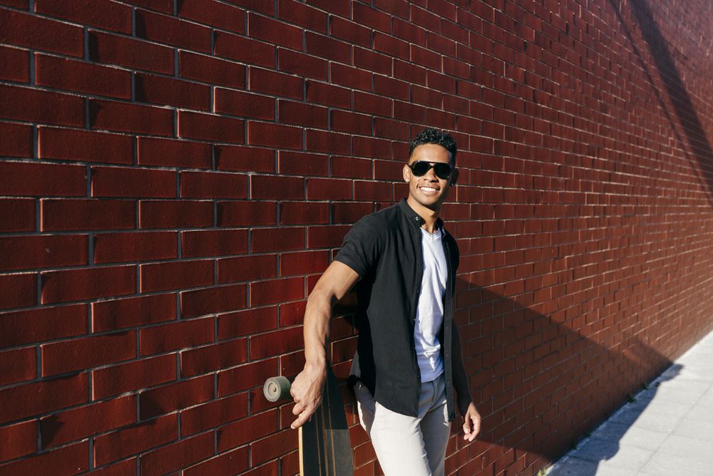 Young Black male with long board leaning on wall