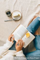 Top view of woman in denim pants reading a book in bed beside a cake 5ooPG5