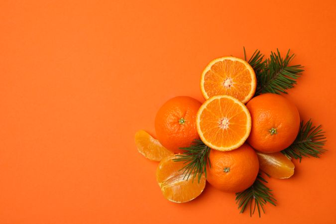 Ripe mandarins and pine branches on orange background, top view