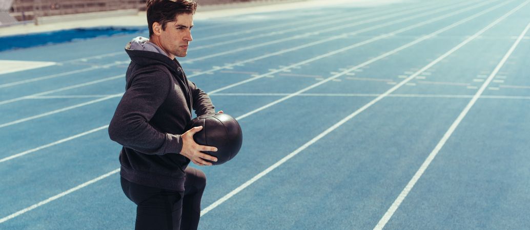 Athlete training with a medicine ball on blue running track