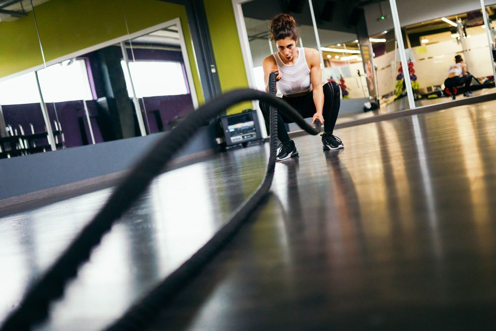 Female working out upper body close to the ground with ropes in gym