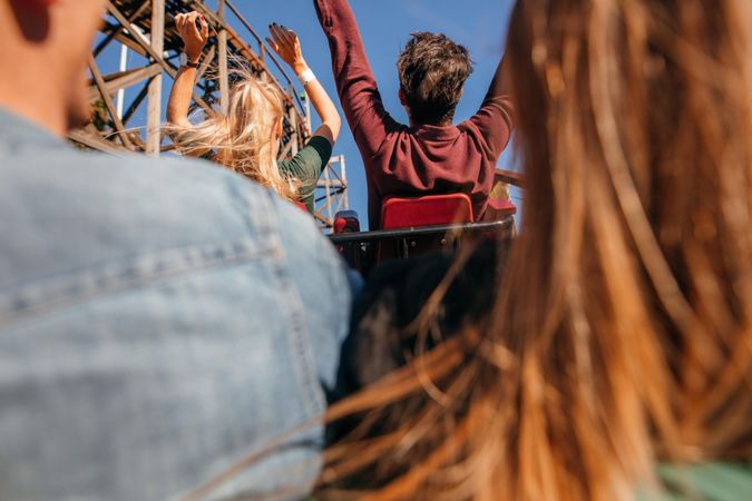 Rear view shot of young friends riding roller coaster ride at amusement park