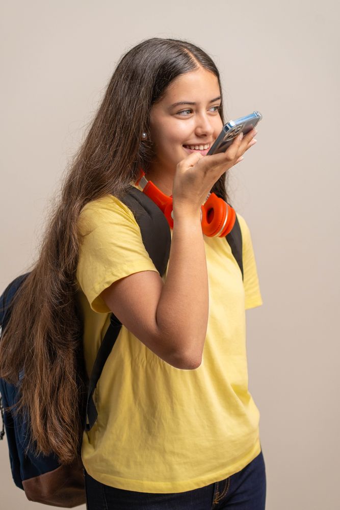 A young student records a voice message or uses a voice assistant on her smartphone.