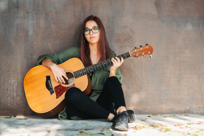 Romantic woman playing guitar leaning on wall