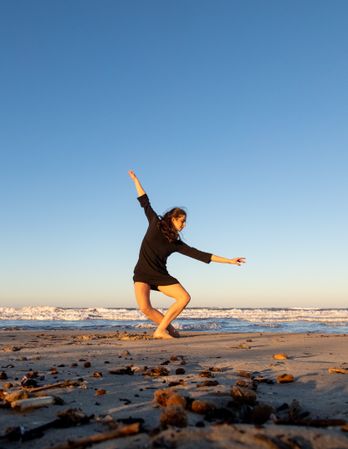 Young woman dancing and posing near water on shore
