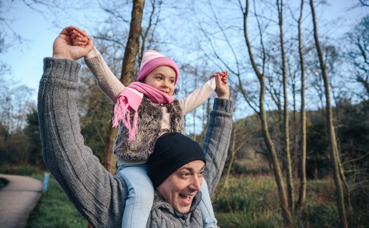 Happy father carrying daughter on shoulders in forest