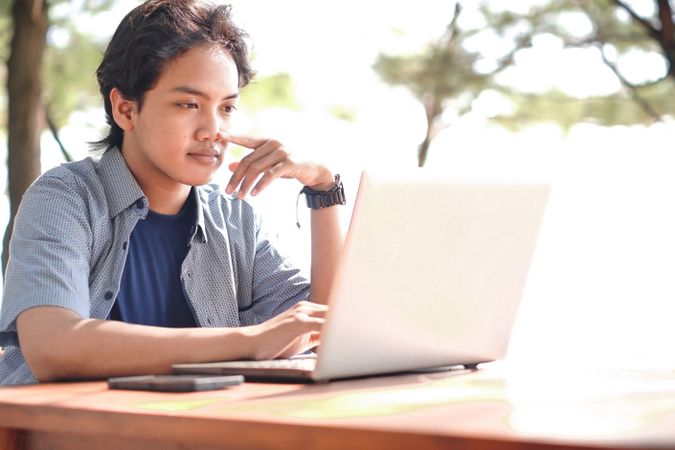 Serious Asian Young businessman work at outdoor with laptop. Concept of remote and freelance work. Young successful man wearing casual blue cloth.