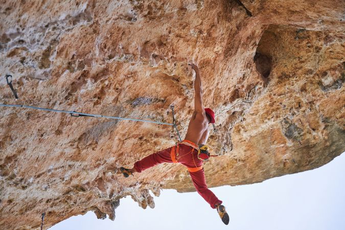 Athletic man climbing on overhanging cliff rock with blue sky ba