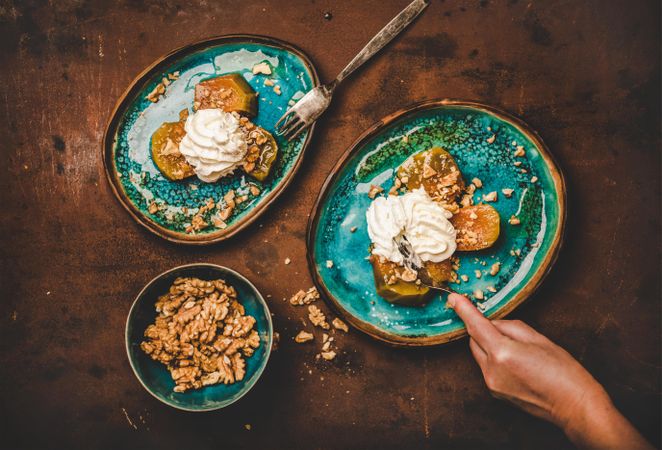 Woman cutting into pumpkin and walnut dessert, with cream and syrup on ocean colored ceramic plates