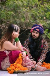 Indian man sitting beside woman in pink sari on ground beside trees bEXOA4
