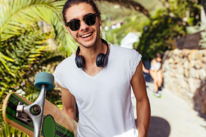 Handsome young man with longboard, wearing sunglasses looking at camera and smiling.