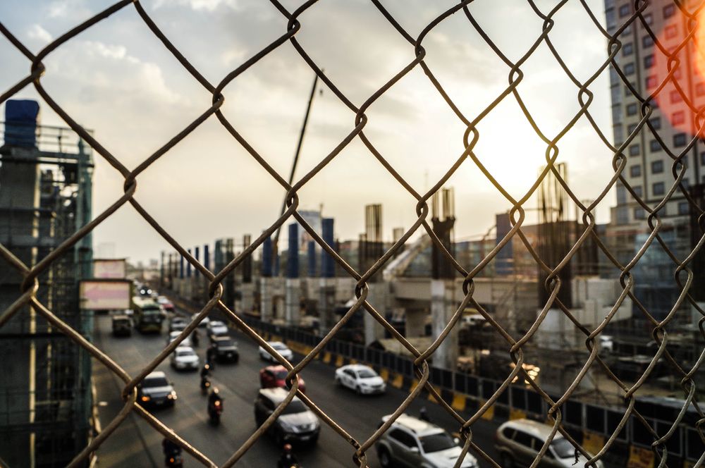 Cars on the road between city buildings through net fence during golden hours