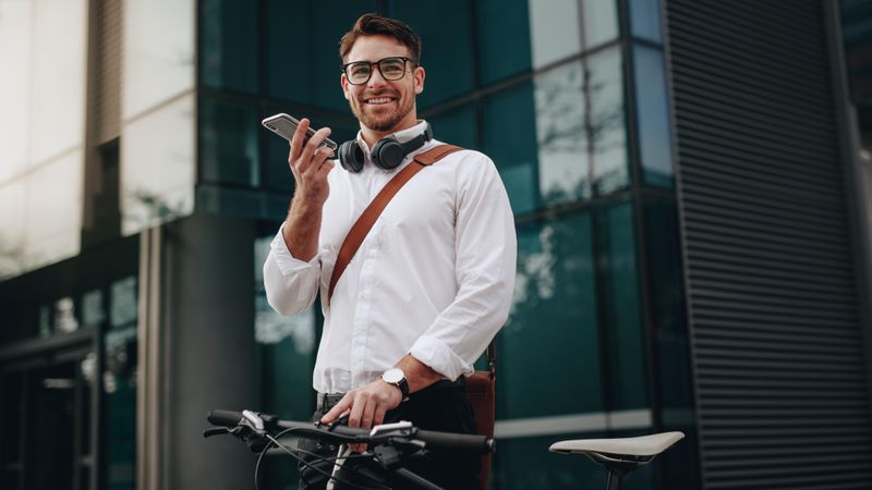 Smiling businessman talking over mobile phone standing on street with his bicycle