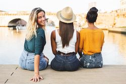 Back of three women sitting on riverbank with one turning around and smiling