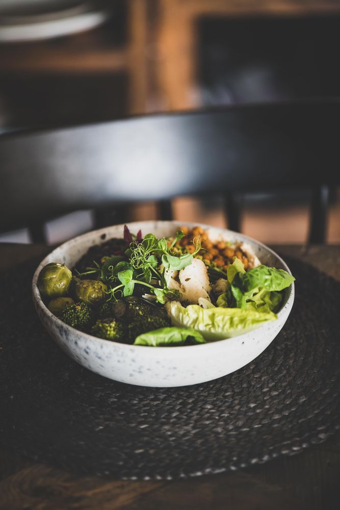 Healthy vegetarian bowl pictured on table with dark chair with smoothie on side, copy space