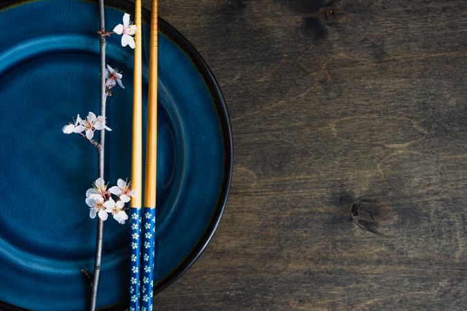 Top view of table setting with chop sticks on ceramic navy plate and delicate cherry blossom branch