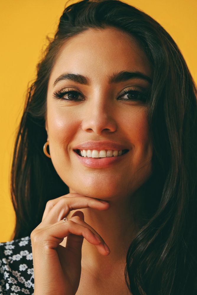Happy Hispanic woman wearing dress standing in yellow room, vertical