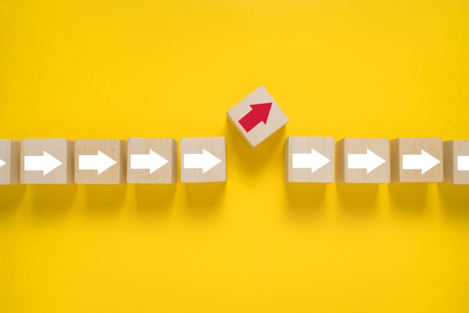 wooden blocks with arrows and one different direction red arrow isolated on yellow background. leadership concept