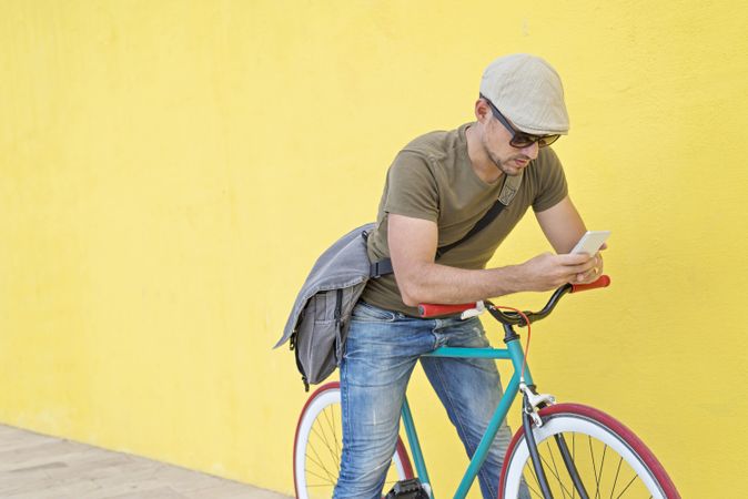 Male in hat and sunglasses texting on phone while sitting on bicycle