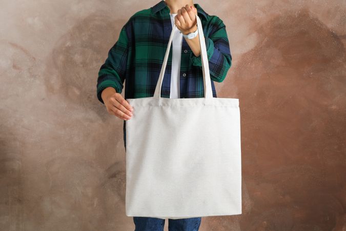 Young woman holding tote bag against brown background, empty space