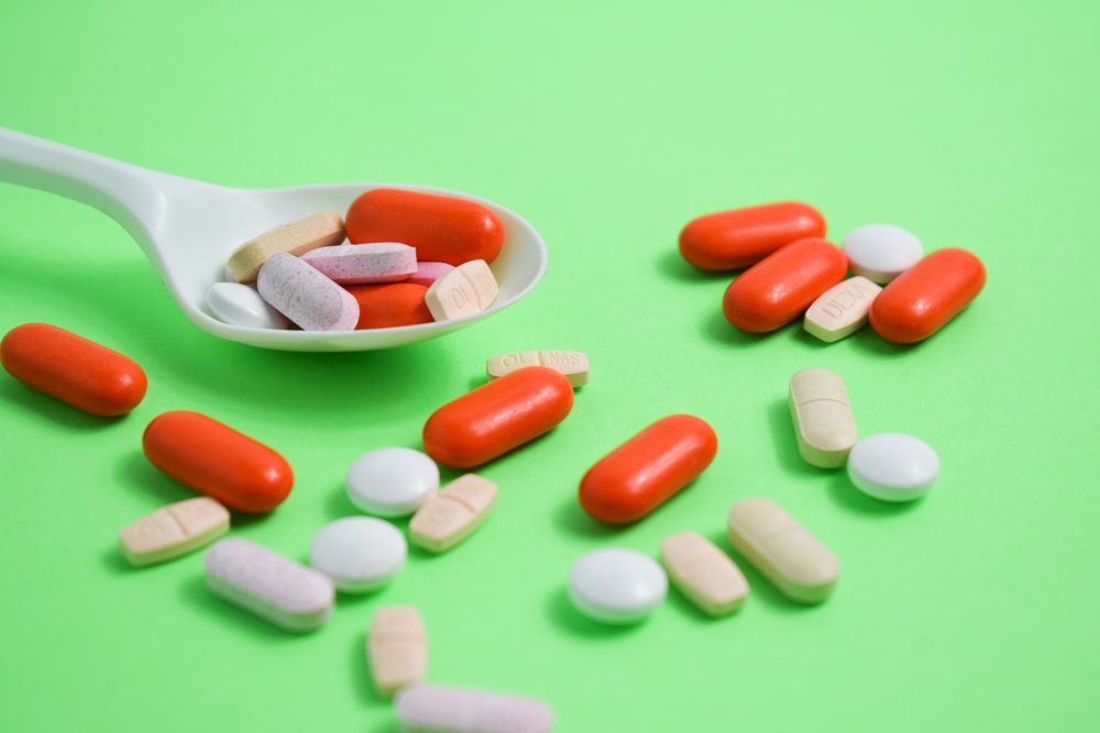 Scattered pills with plastic spoon on green table