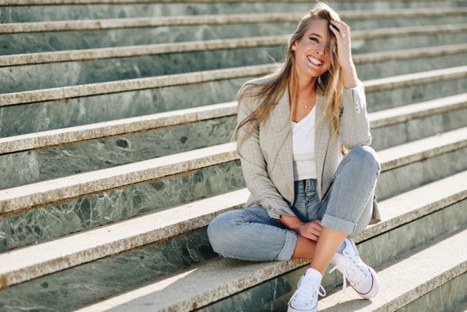 Woman in blazer sitting on outdoor steps on sunny day with hand to head