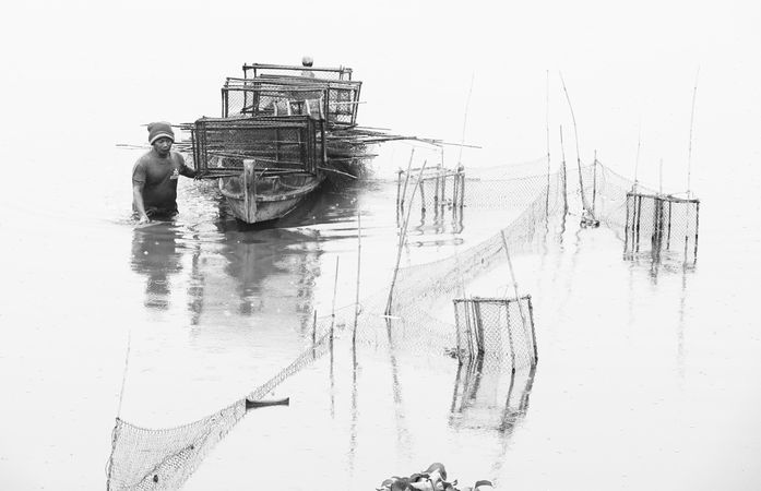 Grayscale photo of man pulling boat on water
