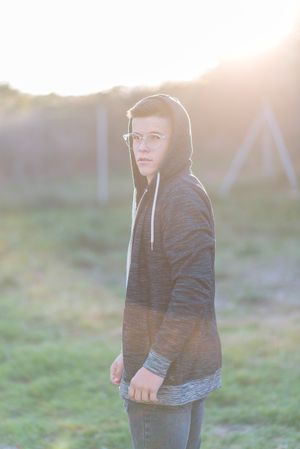 Teenage male in hoodie standing in field