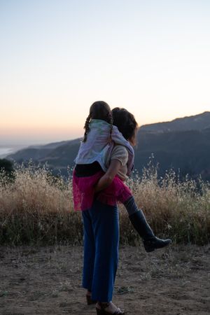 Back view of mother giving daughter a piggy back while looking at view of mountains