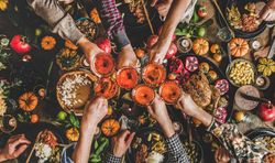 Group of people toasting wine glasses at festive table with roast chicken, squash and pie