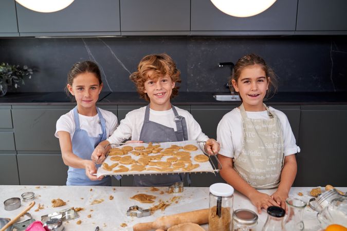 Cheerful children with baking pan of raw cookies
