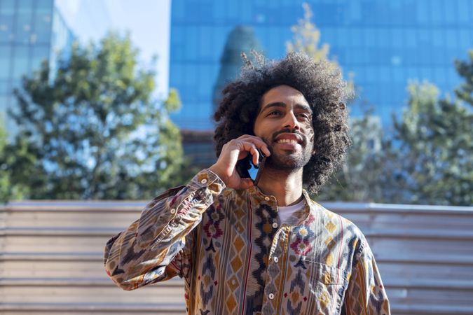 Cool young man talking on a mobile phone while standing outdoors on a sunny day
